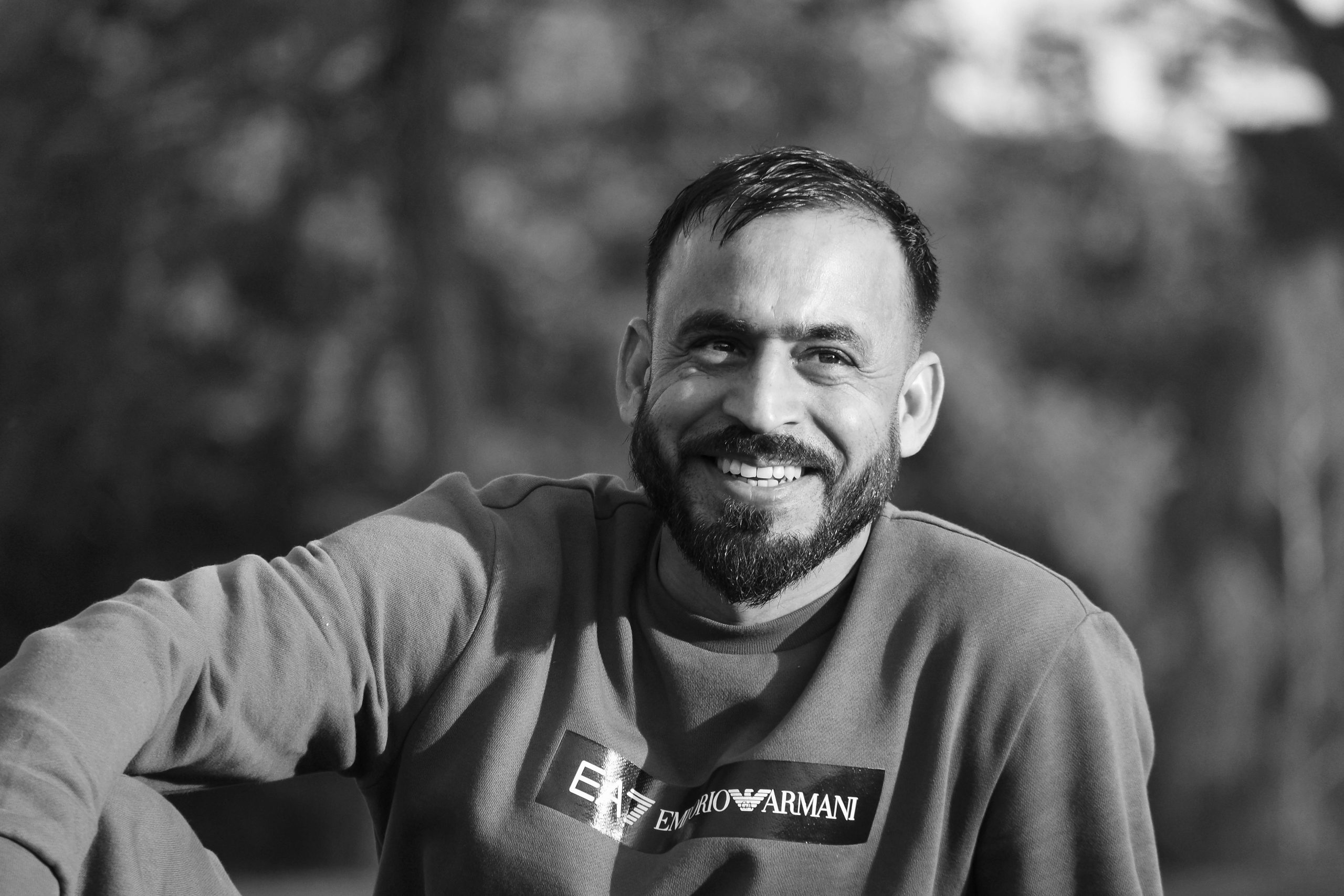 Black and white portrait of a smiling man outdoors, showcasing a relaxed and happy mood.